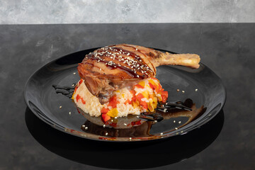 Duck leg in sauce sprinkled with sesame seeds on rice with vegetables.