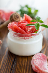 homemade sweet yogurt in a glass jar with pieces of red ripe grapefruit and honey, on a wooden table