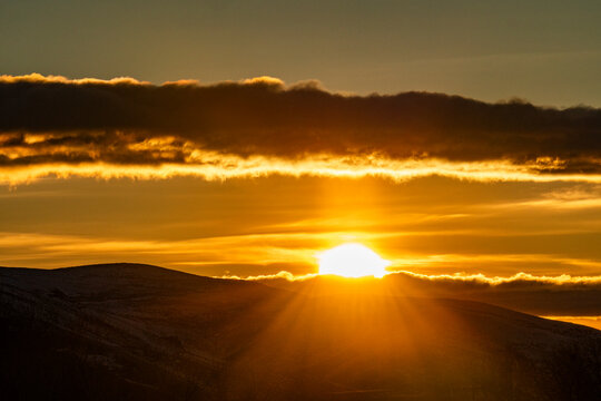 Clouds above golden sun setting behind hills
