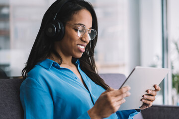 Black woman in headphones enjoying watching tablet touching screen