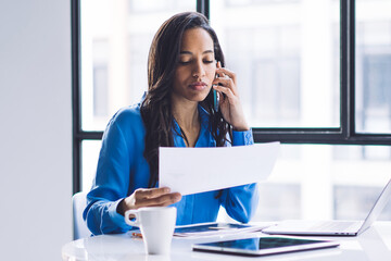 Thoughtful female reading report and browsing laptop in business center