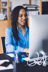 Young African American woman speaking at work place using earphones and computer