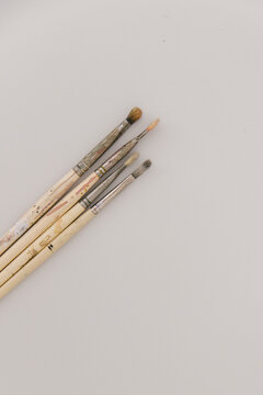 An array of old paint brushes lying on a light grey table.