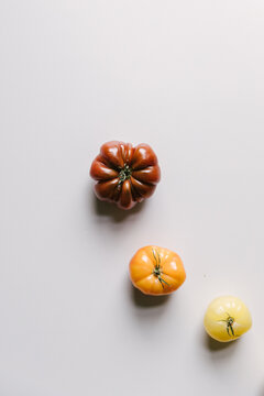 Three different colored and sized tomatoes on a light table top.