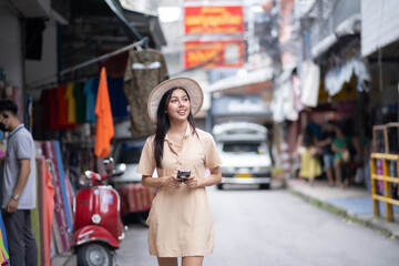 A woman wearing a hat and holding a cell phone walks down a street