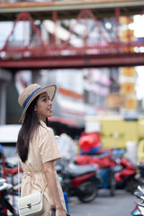 A woman wearing a straw hat and a tan shirt is standing in front of a red bridge