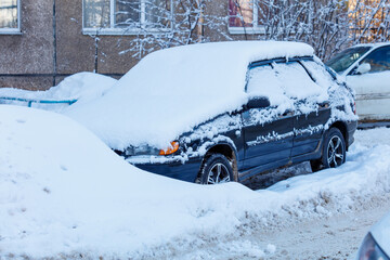 A black car is covered in snow and parked on a snowy street