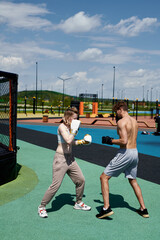 Fototapeta premium Young man and woman training in pair boxing, hitting punching bag, workout outside on sports ground