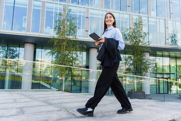 Young Woman Walking Confidently With a Mobile Device Outside a Modern Office Building in Bright Daylight