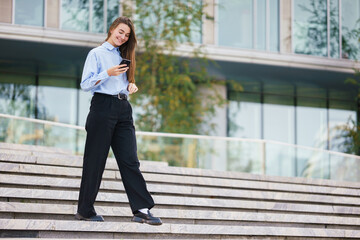 Woman in Casual Attire Smiles While Walking Down Stairs Near a Modern Building During Daytime