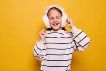 Overjoyed little girl with fur headphones dancing joyfully celebrating triumph and victory feeling...