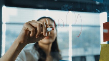 Professional businesswoman writing marketing idea on glass board. Smiling young beautiful project...