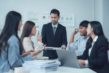 Business Meeting: A diverse team of professionals engaged in a lively discussion, collaborating and brainstorming ideas around a laptop and a stack of documents.