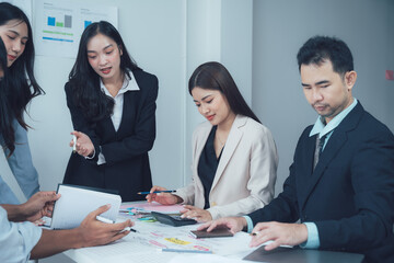 Focused Business Team Collaboration: A diverse group of professionals intently collaborates around a table, reviewing documents and using tablets, showcasing focused teamwork and strategic planning. 