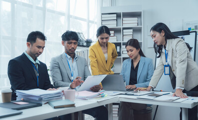 Teamwork Makes the Dream Work: A diverse group of business professionals collaborates intensely around a table, reviewing documents and using laptops in a modern, bright office.