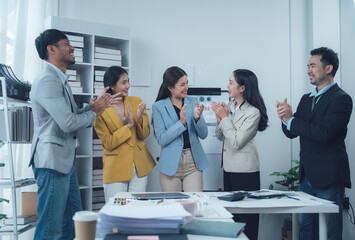 Celebrating Success: A diverse team of business professionals applauds a colleague's achievement in a modern office setting.  The image exudes positivity and shared success.