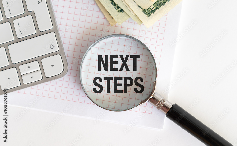 Poster next steps text on magnifying glass with keyboard and open notepad on office desk