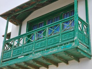 Un balcon en bois peint en vert, avec des motifs sculptés et une patine vieillie, encadrant des...