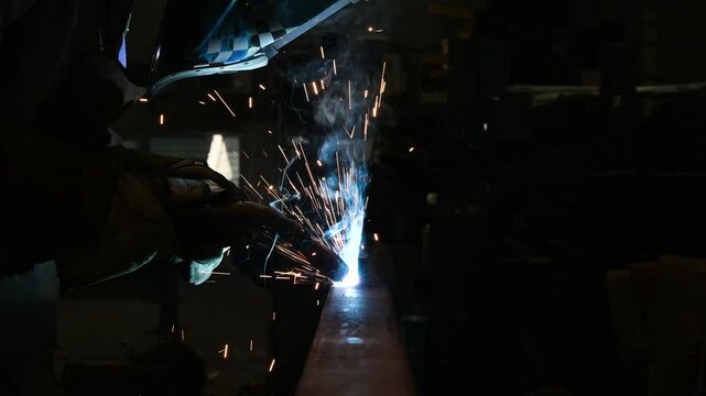 Factory worker welding steel parts together with a welding machine