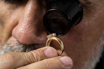 Jewelry appraiser examines a gold ring evaluating large diamond looking through magnifying glass...