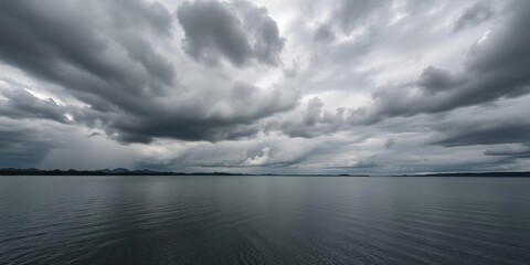 Dark grey clouds gather above a tranquil lake, somber mood, wind-swept trees, darkening sky