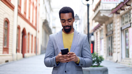 Black man walking down a street, texting on his smartphone