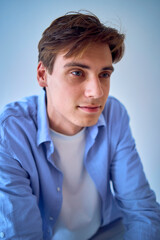 portrait of a handsome young adult man in a blue shirt sitting on a chair on a blue background
