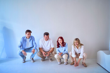 Naklejka premium a family, middle-aged husband and wife, young adult son and teenage daughter, squatting on a white background, studio photo shoot