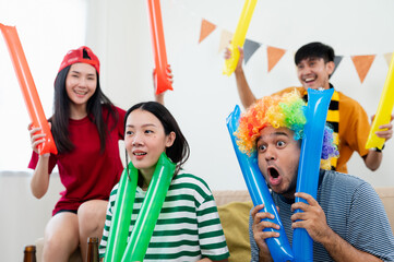 Fototapeta premium A group of Asian male and female friends are excited and happy to watch the World Cup match on TV. and eat snacks together at home Sports fans shout and celebrate the victory of their sports team.