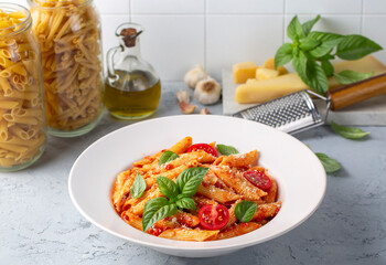 Classic italian pasta penne alla arrabiata with basil and freshly grated parmesan cheese on dark table. Penne pasta with chili sauce arrabbiata.