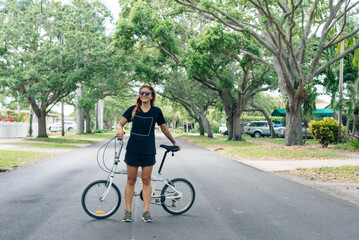 Naklejka premium Teen student girl or young woman in black dress with a folding bicycle on the road