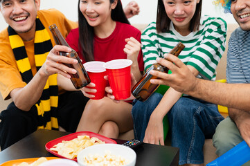 A group of excited Asian male and female friends watched the World Cup match on TV and drank beers and ate snacks together at home. Sports fans shout and celebrate the victory of their sports team.