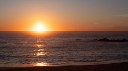 Fototapeta premium Sun dropping below horizon at sunset over the ocean, with sunlight reflected on the waves. Copy space on right.