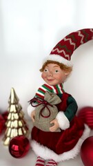 Home xmas decorations. Charming Christmas Elf Holding Gift Bag Amid Festive Decor. Adorable Christmas elf figurine holding a small gift bag, surrounded by holiday decorations including a gold tree