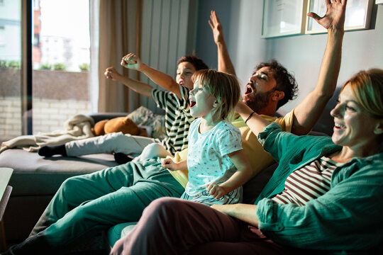 Family cheering while watching tv at home on the couch - Powered by Adobe