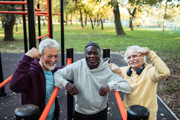 Senior men flexing muscles after outdoor workout at park fitness station