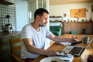 Man managing bills with laptop on kitchen desk