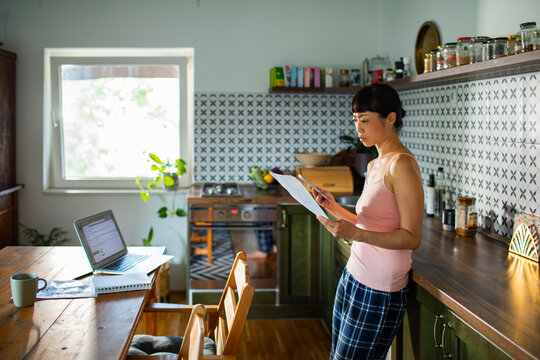 Stressed woman managing bills with laptop on kitchen desk