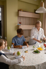 A mother and her children prepare healthy lunches in a cozy kitchen. The table is filled with nutritious food, and the family collaborates in the morning routine.
