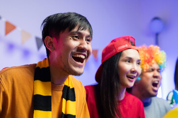 A group of excited Asian male and female friends watched the World Cup match on TV and drank beers and ate snacks together at home. Sports fans shout and celebrate the victory of their sports team.