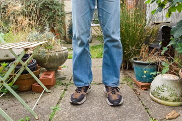 legs of a man standing in the yard wearing jeans and sneakers