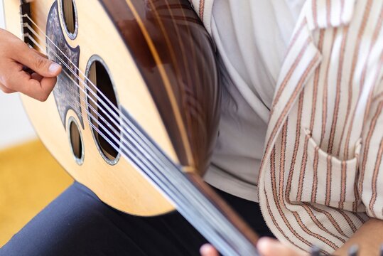 A detailed view of a musician&rsquo;s hand strumming the strings of atraditional oud instrument