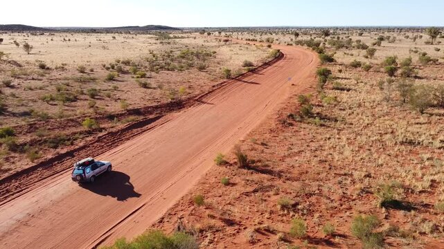 Aerial video of a car driving in the middle of the outback. Long sandy road with little bushes on the side. 4wd adventure in the red centre of Australia. Driving along a dirt road.