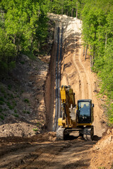Yellow excavator against the background of a trench with pipes. Laying a pipeline through a hilly forest.