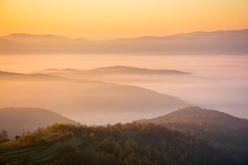 mountainous landscape with fog in the valley. sunny morning. countryside scenery in fall season. glowing mist between rolling hills