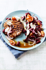 Grilled pork steak with Kidney bean, cherry tomatoes, onion and feta cheese on bright wooden background
