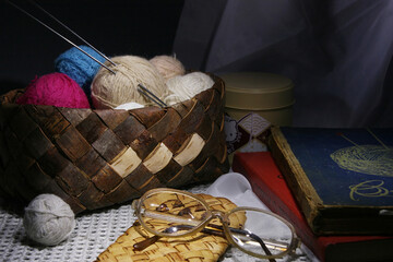 Still life with multi-colored balls of thread and knitting needles in a wicker birch bark box, old...
