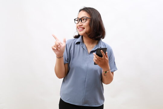 Excited young asian woman shopping on mobile app, holding phone and pointing finger left at empty copy space, showing promo text, standing with smartphone against white background