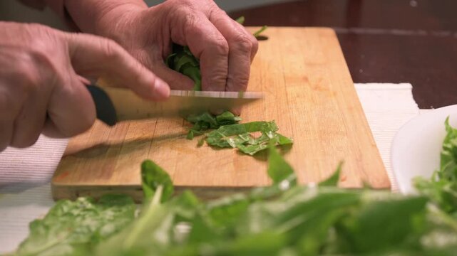 An elderly woman cutting sorrel on a cutting board. 