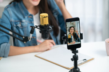 Host channel Asian influencer talking in broadcast wearing headsets on social media live on smartphone recording online, greeting listeners with coaching life or business at modern studio. Stratagem.